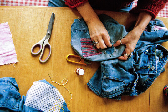 Woman mends a pair of jeans sewing with embroidery thread