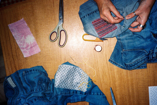 Film flash moment of anonymous woman mending a pair of jeans at home