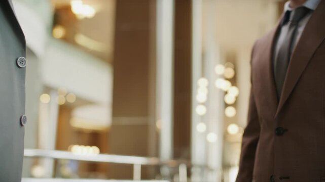 Close up view of two diverse unrecognizable businessmen in formal suits shaking hands during meeting in high-end hotel lobby