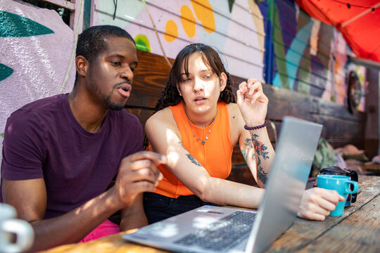 Two coworkers brainstorming on laptop at colorful outdoor cafe