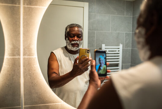 Senior man video calling while shaving in bathroom