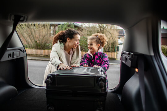 Mother and daughter loading suitcase into car trunk on suburban street
