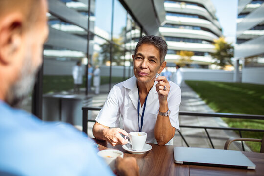 Senior nurse talking with colleague during coffee break in hospital courtyard