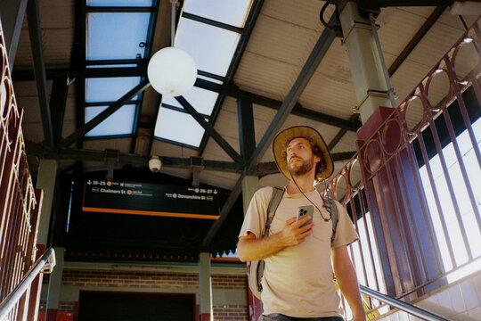 Man with smartphone navigating sunlit train station, shot on film 