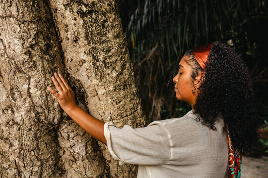 Young woman leans her forehead against a large tree trunk in a quiet moment of reflection