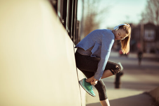 Young woman tying running shoe on city street