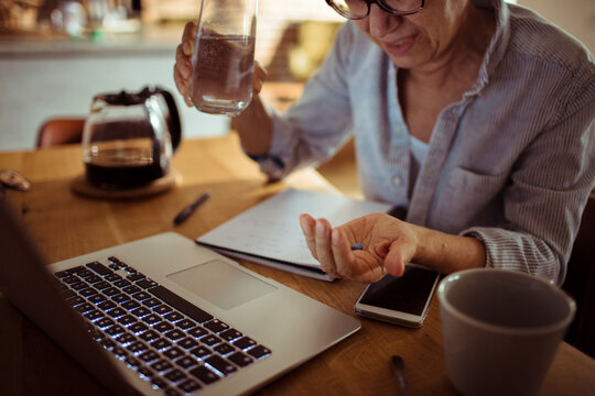 Mature woman taking medication at home office desk