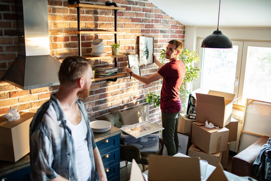 Two men decorating and unpacking in a brick wall apartment kitchen