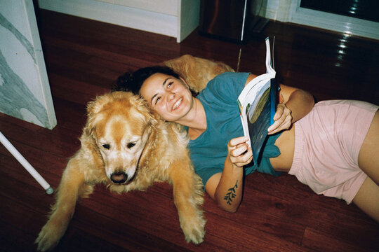 Woman reading book while bonding with the dog at home. Shot on film 