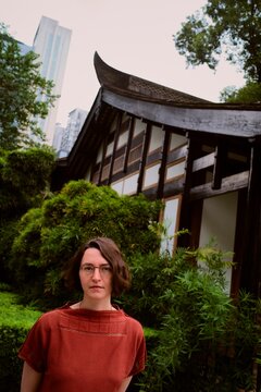 Woman Stands in Garden Near Traditional Building in Urban Area