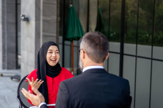 Two business professionals, including a Muslim woman wearing a Islam hijab, discussing work on a tablet at an outdoor caf&eacute;.