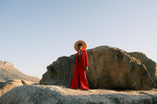 Young man in red clothing and straw hat posing on coastal rocks
