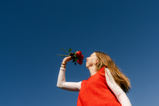 happy young woman with red top smelling  red roses 