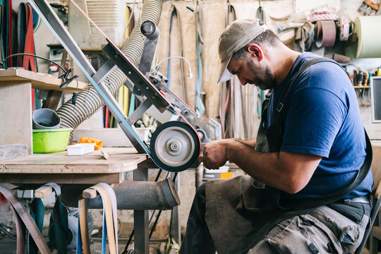 Craftsman grinding knife blade in workshop using belt sander