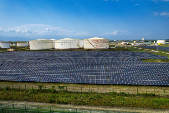 Aerial view of the hydrocarbon and LPG storage facility featuring large white tanks and a vast solar panel array under a blue sky in Volpiano, Piemonte, Italy.
