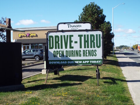 Nepean, Ontario, Canada &ndash; July 27, 2025: A roadside sign advertises that the "Panera Bread" drive-thru remains open during renovations, with a Booster Juice store nearby on W Hunt Club Rd.
