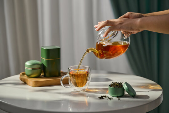 Tea is being poured into a clear cup with tea leaves