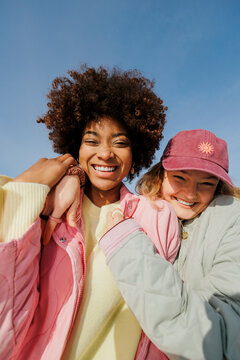 Two smiling teens hugging together under blue sky