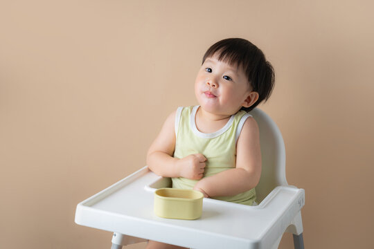 Adorable baby sitting in a high chair with a small bowl