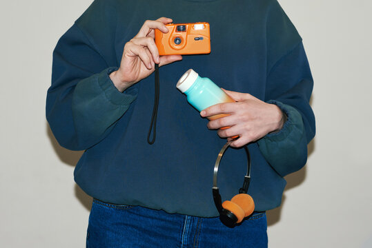 Woman holding camera, reusable bottle and headphones