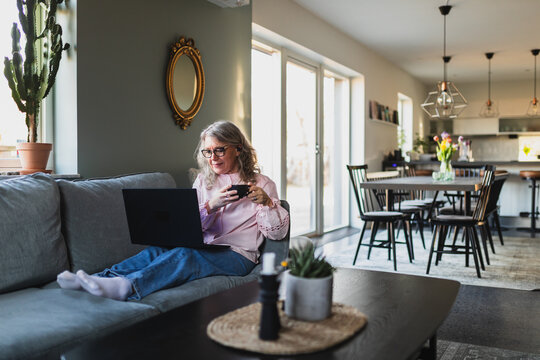 Woman working on laptop while relaxing on sofa in modern home
