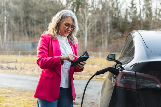 Woman using smartphone app while charging electric car