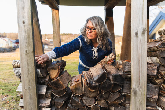 Mature woman stacking firewood in outdoor wooden shed