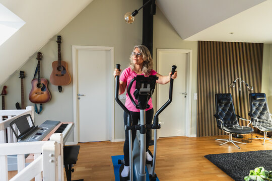 Mature woman exercising on elliptical machine in bright home gym