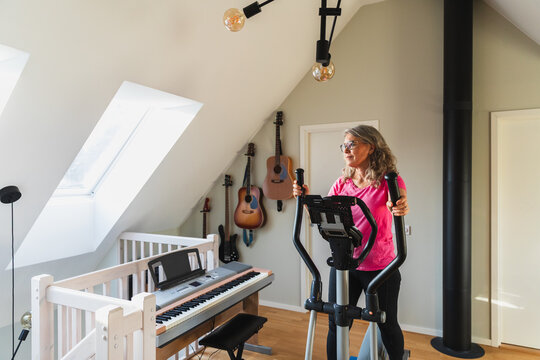 Mature woman exercising on elliptical machine in bright home gym