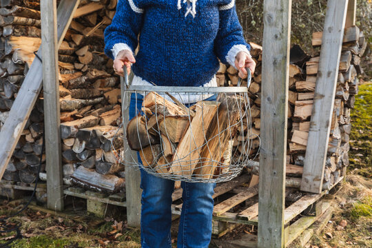 Person carrying metal basket full of firewood from outdoor shed