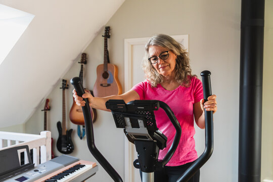 Mature woman exercising on elliptical machine in bright home gym