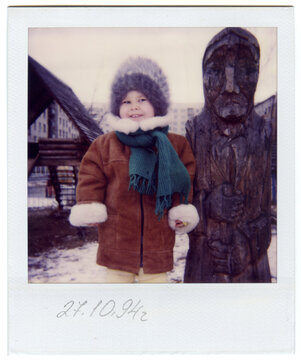 Vintage Polaroid of a Toddler in Fur Hat by Wooden Sculpture in Winter