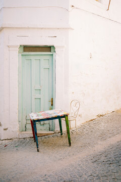 Old wooden table and an iron chair on street in front of green door 