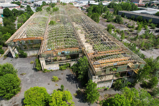 Aerial view of an abandoned industrial site with skeletal roof structures and overgrown vegetation in Settimo Torinese, Piedmont, Italy.