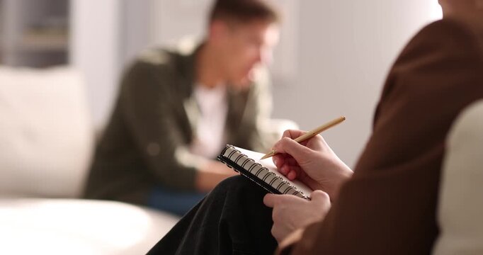 Professional psychologist making notes during therapy session with patient indoors, selective focus