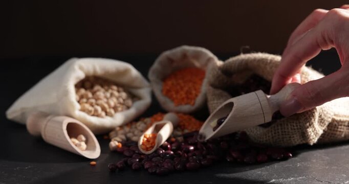 Woman taking scoop with dried red beans and other legumes at black table, closeup