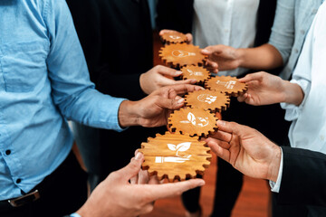 Naklejka premium A close-up view of diverse hands holding wooden gears, each marked with eco-friendly symbols. This image showcases teamwork in promoting sustainable business practices and growth. Amity