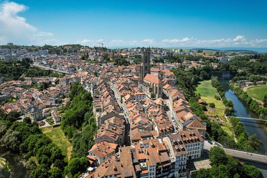 Aerial view of the historic old town featuring St. Nicholas Cathedral, traditional red-tiled rooftops, and the Sarine river valley Fribourg, Fribourg, Switzerland.