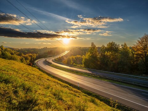 Empty asphalt highway winding through forested landscape in autumn colors at sunset