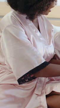 Vertical video: Turning mother in pink robe tending daughter's hands on bed for care, blue bonnet