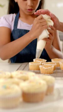 Vertical video: Seeing frosted cupcakes, aproned youth piping with bag in kitchen, adult guiding