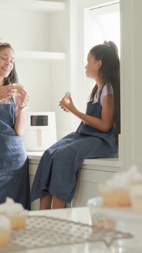 Vertical video: Showing cupcake, mother guiding daughter tasting frosting in kitchen, denim aprons