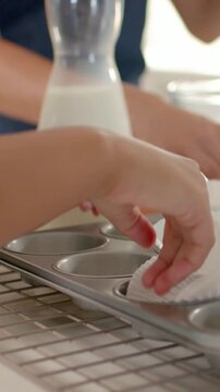 Vertical video: Baking, mom and child placing liners in tray for batter in kitchen in dark tops