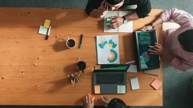 Top view of skilled project manager talking about financial graph to investors while sitting at meeting table with data analysis document. Diverse team discussing and brainstorming idea. Convocation.