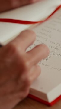 Person Writing a Grocery List in Red Notebook