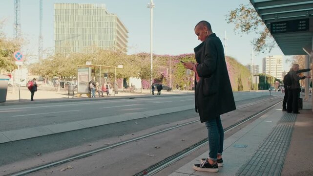 Woman Using Mobile Phone While Waiting at City Tram Stop