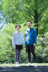 Obraz premium 新緑の公園でウォーキングや散歩を楽しむミドル夫婦の正面全身カメラ目線で笑顔