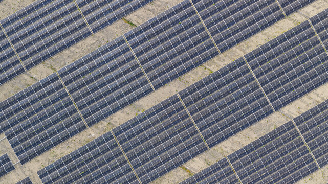 Aerial view of Zonnepark Braambergen solar farm with rows of photovoltaic panels arranged in geometric patterns on sandy ground in Almere, Flevoland, Netherlands.