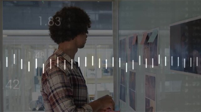 Designer studying grid on glass planning layout placing notes while using phone waveforms reacting