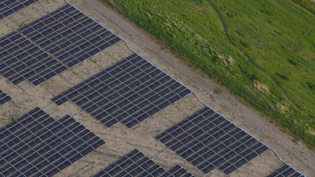 Aerial view of Zonnepark Braambergen solar farm with rows of photovoltaic panels on sandy soil next to a green grassy slope in Almere, Flevoland, Netherlands.